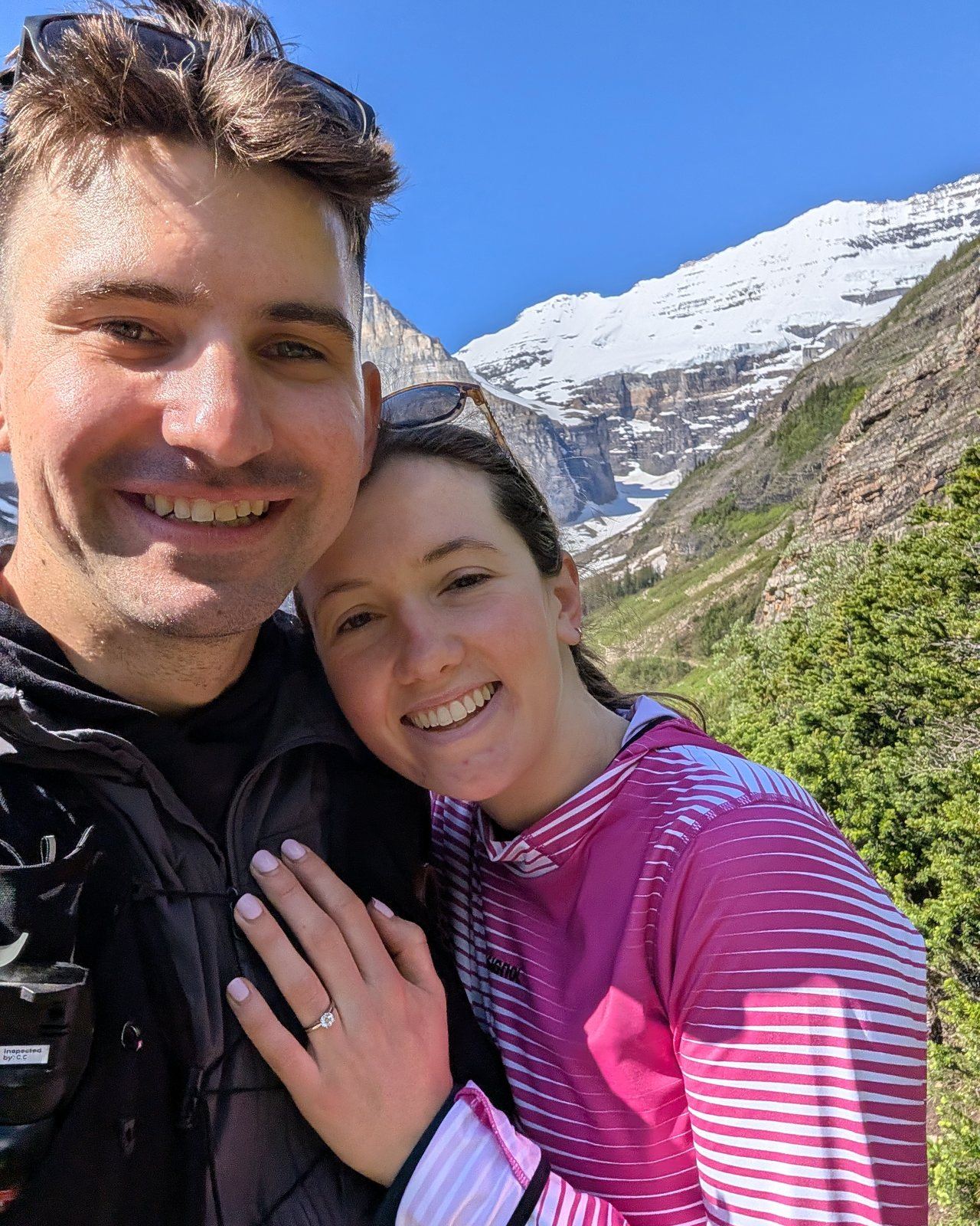 Katrin and Rob smiling on a mountain trail, Katrin's hand with her engagement ring resting on Rob's chest