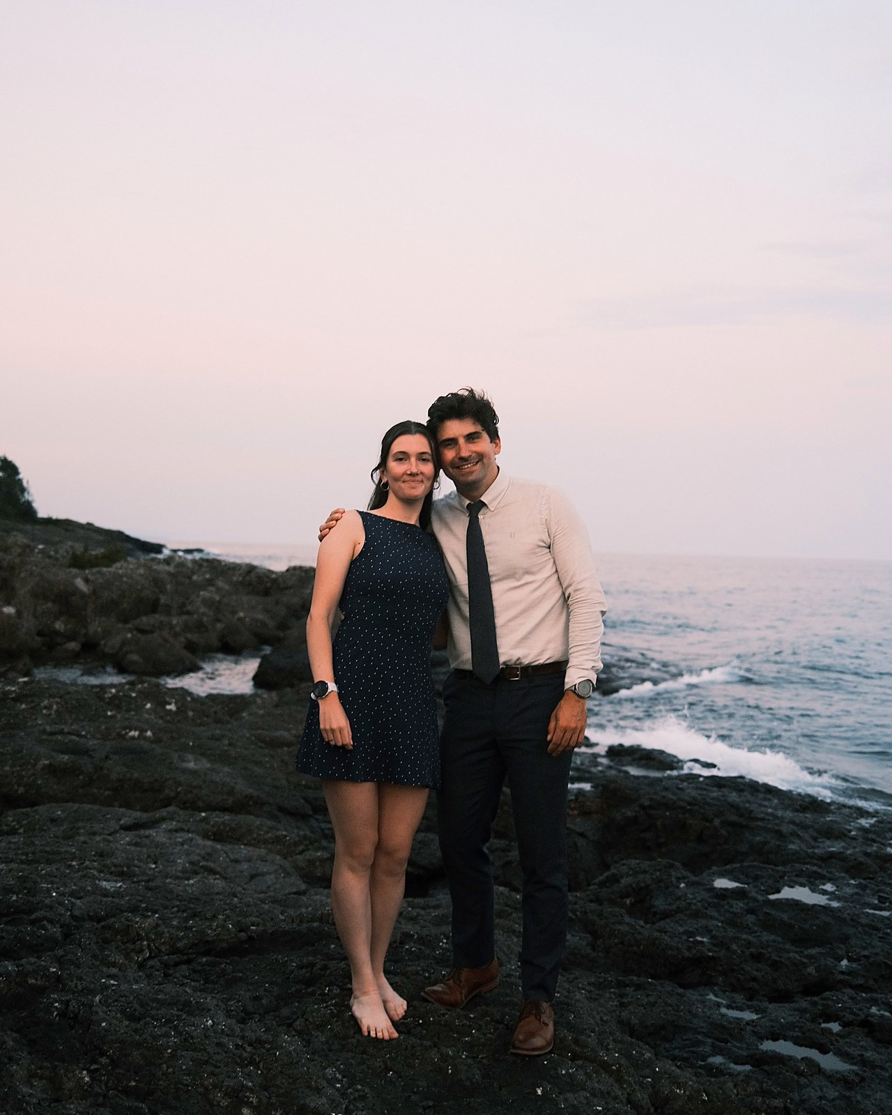 Katrin and Rob standing together on the rocky shore of Lake Superior at dusk